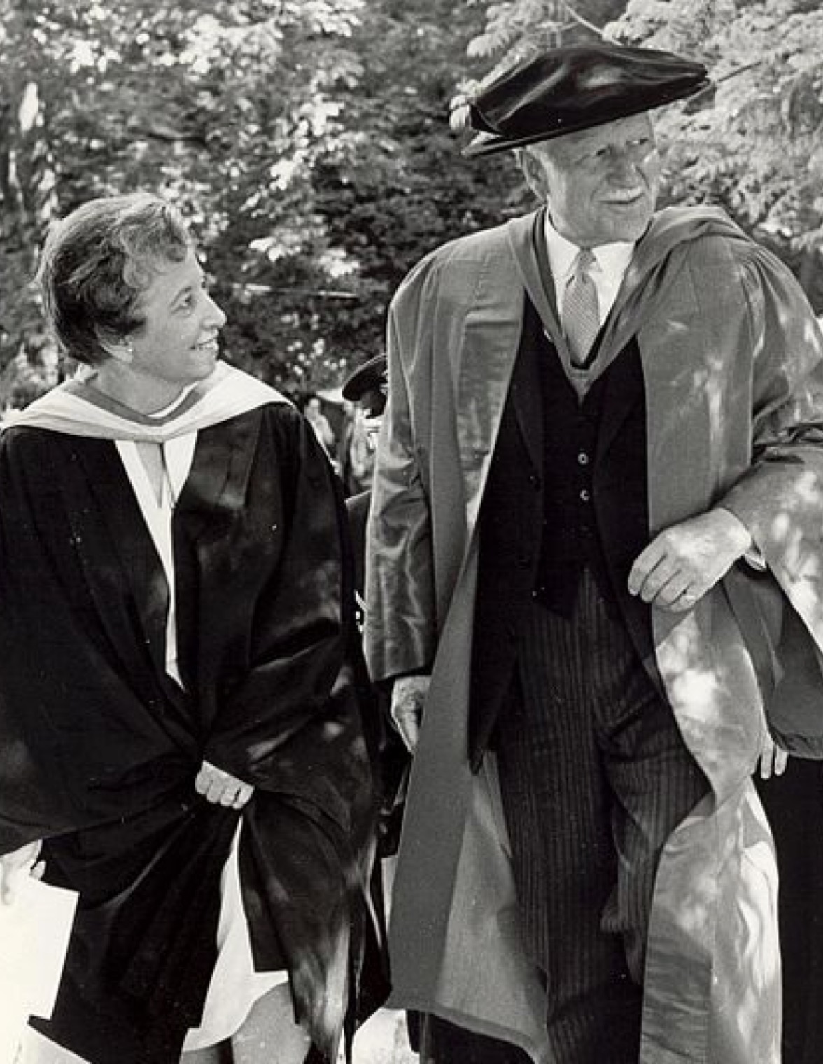 Une femme et un homme marchent côte à côte. Tous deux sont vêtus de robes académiques.